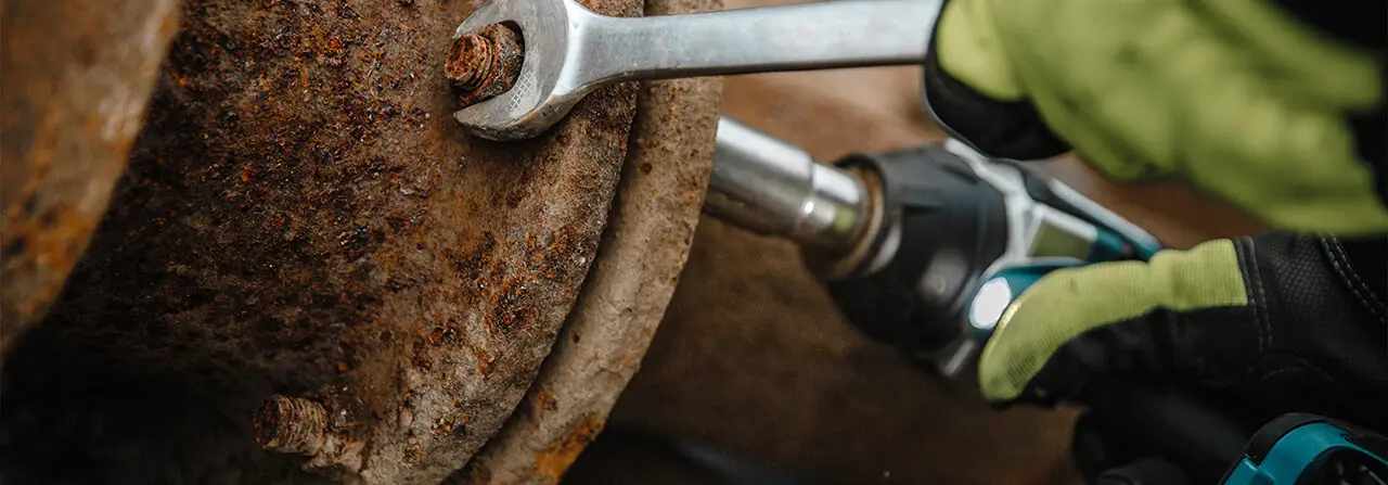 Arbeit an einer verrosteten Rohrverbindung mit Schraubenschlüssel und Akkuschrauber